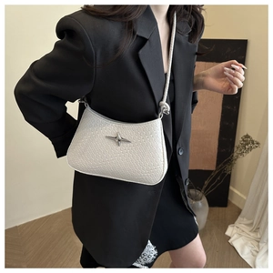 Close-up of white woven underarm bag with silver star buckle worn with black blazer