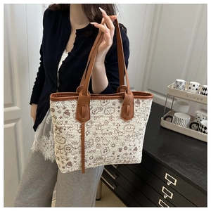 Close-up of beige woven tote bag featuring brown cartoon patterns and slim leather straps