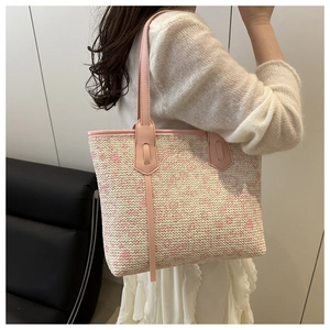Detail view of a pink and white woven tote bag with leather straps on a female model