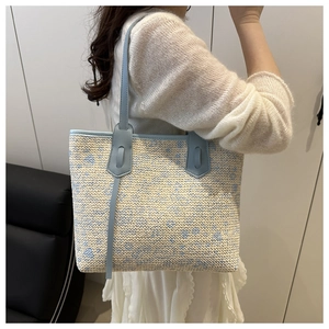 Detail of woven straw tote bag with blue floral patterns and light blue leather straps