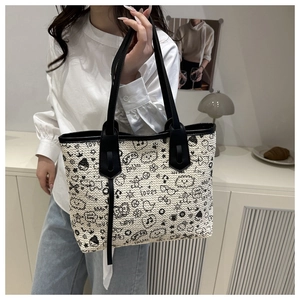 Detail of woven tote bag featuring black cartoon graffiti patterns and long leather handles