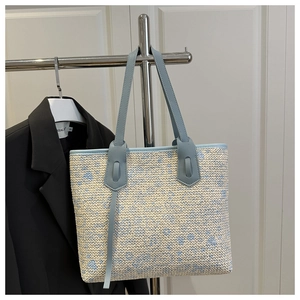 Detail of blue and beige woven tote bag showing floral texture and leather shoulder straps