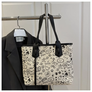 Close-up of a woven tote bag with cartoon graffiti and black leather straps details
