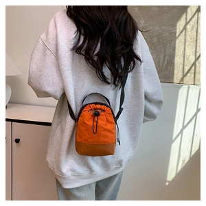Detail view of the drawstring bucket bag featuring orange canvas and brown leather base
