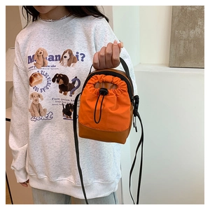 Detail of orange drawstring crossbody bag with adjustable strap and contrast base