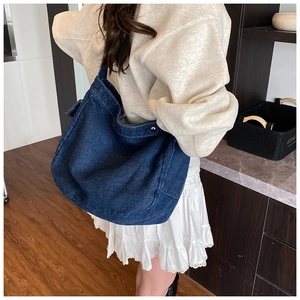 Dettaglio della borsa a tracolla in denim blu scuro con cuciture a contrasto e rivetti