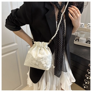 Detail of elegant white lace bucket bag with pearl strap and floral drawstring texture