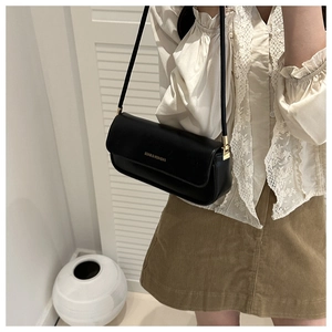 Detail of a black leather baguette bag with golden logo and slender shoulder strap