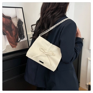 Detailed view of cream bow shoulder bag featuring silver chain strap and metal logo