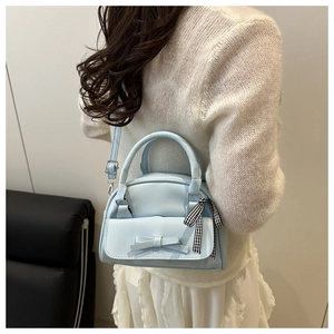 Light blue shell bag with bow and checkered ribbon shown on a model's shoulder