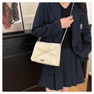 Model wearing a cream leather chain bag with 3D bow decoration and silver metal strap