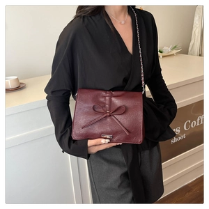 Detailed side view of a burgundy chain bag featuring a leather bow and metal buckle clasp