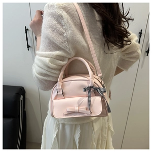 Detail of pink bow handbag with plaid ribbon charm shown on a model in home setting