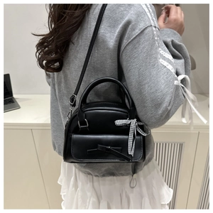 Detail of black matte leather square bag with bow accents worn by a model in casual style