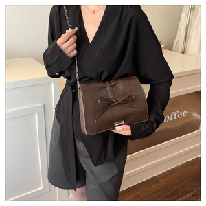 Detail of dark brown shoulder bag with a large bow decoration and silver chain strap