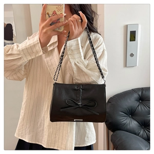 Detail of black faux leather shoulder bag with metallic chain and large bow decoration