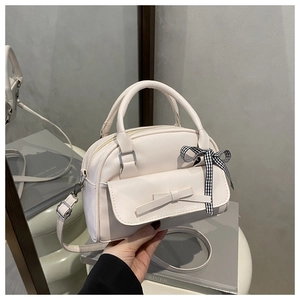 Close-up of off-white Boston bag with leather bow and checkered ribbon on a side table