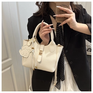 Detailed view of white pebble leather tote bag with gold hardware and dog charm