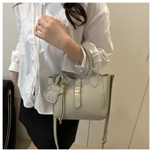 Detail of light grey lychee leather tote with gold buckle and dog charm on a model