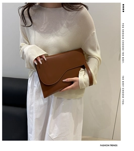 Detailed view of brown leather clutch with unique wavy flap and matching hand strap