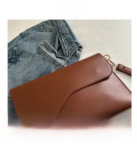 Macro shot of a minimalist brown leather envelope bag with a wavy flap and golden hooks