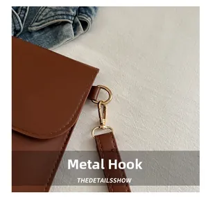 Close-up of golden metal hooks and precise stitching on the brown leather handbag