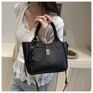 Detailed shot of black pebbled leather tote featuring gold twist lock and dog charm