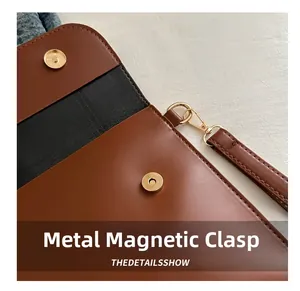 Detail of brown leather envelope bag featuring golden magnetic hardware buckles and wristlet