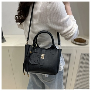 Detail of black pebbled leather tote bag with metallic lock and cute dog charm pendant
