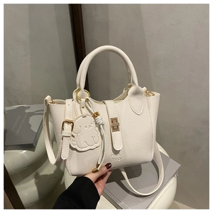 Close-up of white lychee-patterned leather tote with gold buckle and cute poodle charm