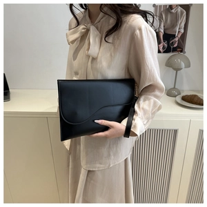 Detail of black envelope clutch with asymmetric flap and matching wrist strap