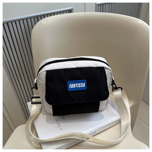 Détail du petit sac carré minimaliste avec rabat contrasté et étiquette de marque bleue