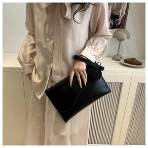 Close-up of minimalist black envelope handbag with smooth leather texture and gold buckle