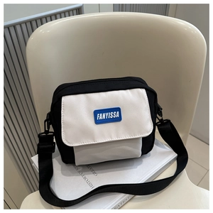 Détail d'un sac à bandoulière minimaliste noir et blanc avec étiquette FANYISSA sur chaise