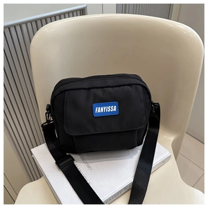 Détail d'un sac bandoulière en nylon noir avec étiquette logo bleue et boucle réglable