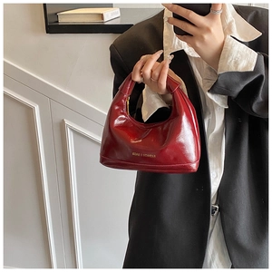 Detail of red patent leather dumpling bag with gold fashion lettering and handle