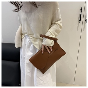 Close-up of caramel brown leather envelope clutch with top handle on white outfit