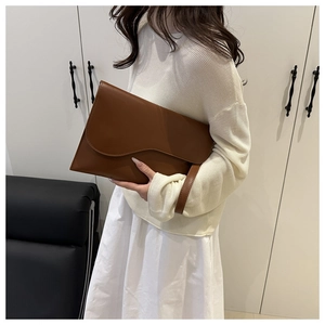 Close-up of brown leather envelope bag featuring a stylish wavy edge and hand strap