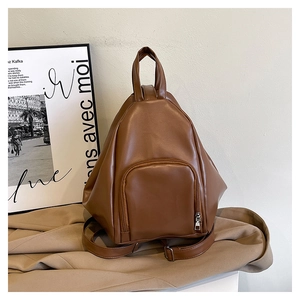 Detail view of a caramel brown leather backpack on beige fabric with art background