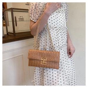 Détail de la pochette en paille tissée avec bandoulière chaîne dorée et fermoir métal