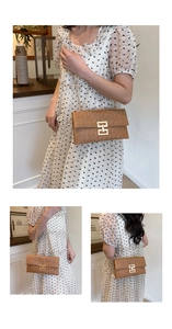 Detail of woven straw envelope bag featuring a gold metal H-clasp and chain strap