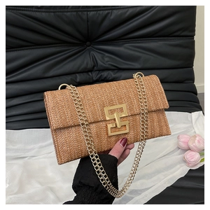Détail de la pochette en paille tissée avec chaîne dorée et fermoir géométrique doré