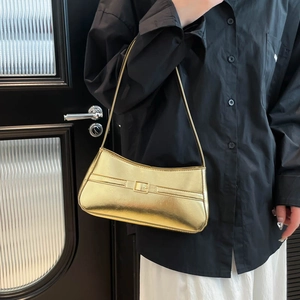 Metallic gold baguette shoulder bag with decorative buckle strap worn by a female model