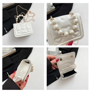 Close-up of white heart-embossed bag featuring pearl handle and gold chain details
