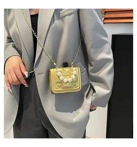 Detail of a mini gold heart embossed handbag with pearl handle and metal chain strap