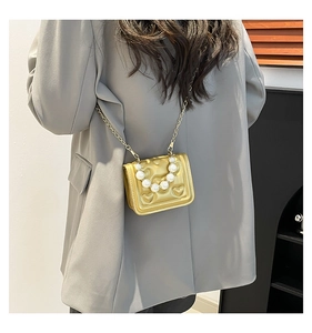 Detail of gold heart-quilted crossbody bag featuring a large pearl handle and metal chain