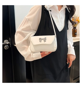 Close-up of elegant white baguette bag with a silver metal bow buckle on a model
