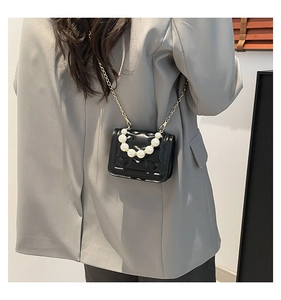 Detail of heart-embossed black patent leather bag with white pearl handle and chain
