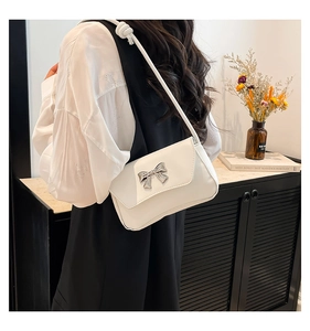 Close-up of white shoulder bag with silver bow ornament and leather flap texture