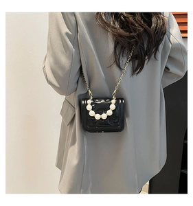 Detail of a black quilted heart pattern bag with pearl handle on a model's shoulder